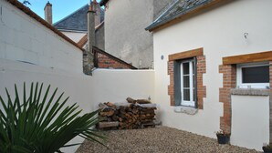 A courtyard with a gravel ground, a stack of firewood, a white wall, and a small window with a brick frame. - IDEAL FAMILY HOUSE (Bracieux)