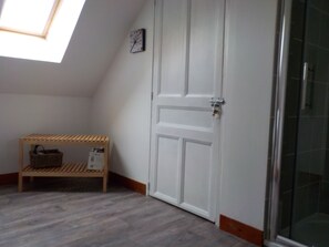Una habitación con techo inclinado, una puerta blanca, un pequeño banco de madera con una cesta y una puerta de ducha de vidrio.