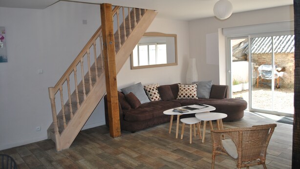 A living room with a wooden staircase, a brown sofa, a white coffee table, and a wicker chair. - IDEAL FAMILY HOUSE (Bracieux)