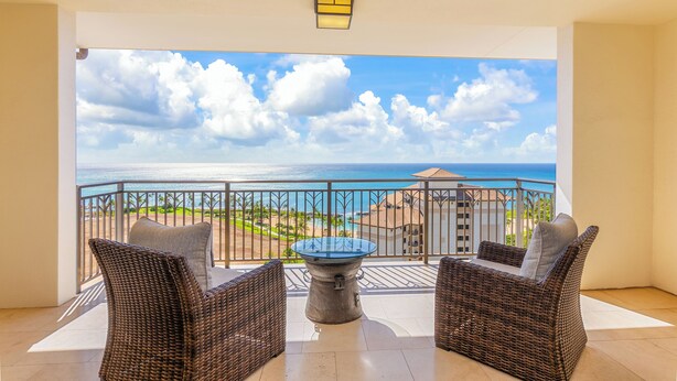 Ein Balkon mit Korbmöbeln, einem Glastisch und Blick auf das Meer und Gebäude.