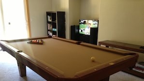 Une table de billard avec une seule boule blanche, une bibliothèque et un téléviseur dans une pièce dont le sol est recouvert de moquette.