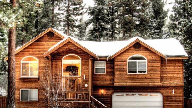 Une cabane en rondins avec un porche à l’avant, un garage et un paysage enneigé.