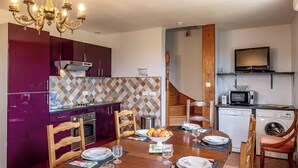 A compact kitchen with a microwave, stove, and dishwasher, a dining table set with plates and glasses, and a chandelier.
