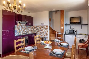 A compact kitchen with a microwave, stove, and dishwasher, a dining table set with plates and glasses, and a chandelier.