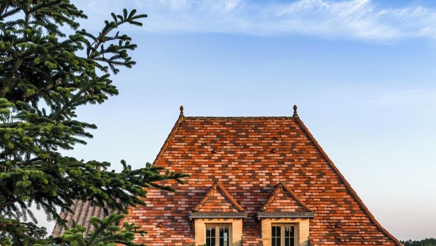 A stone building with a tiled roof, a patio with a table and chairs, and a Christmas tree.
