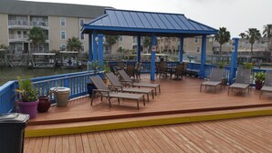 Une terrasse extérieure couverte, dotée de chaises longues et de tables, qui offre une vue sur une étendue d’eau et des immeubles résidentiels.