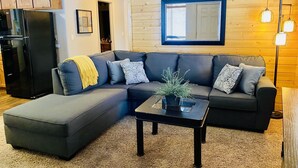 A modern living room with a sectional sofa, a coffee table, and a black refrigerator.
