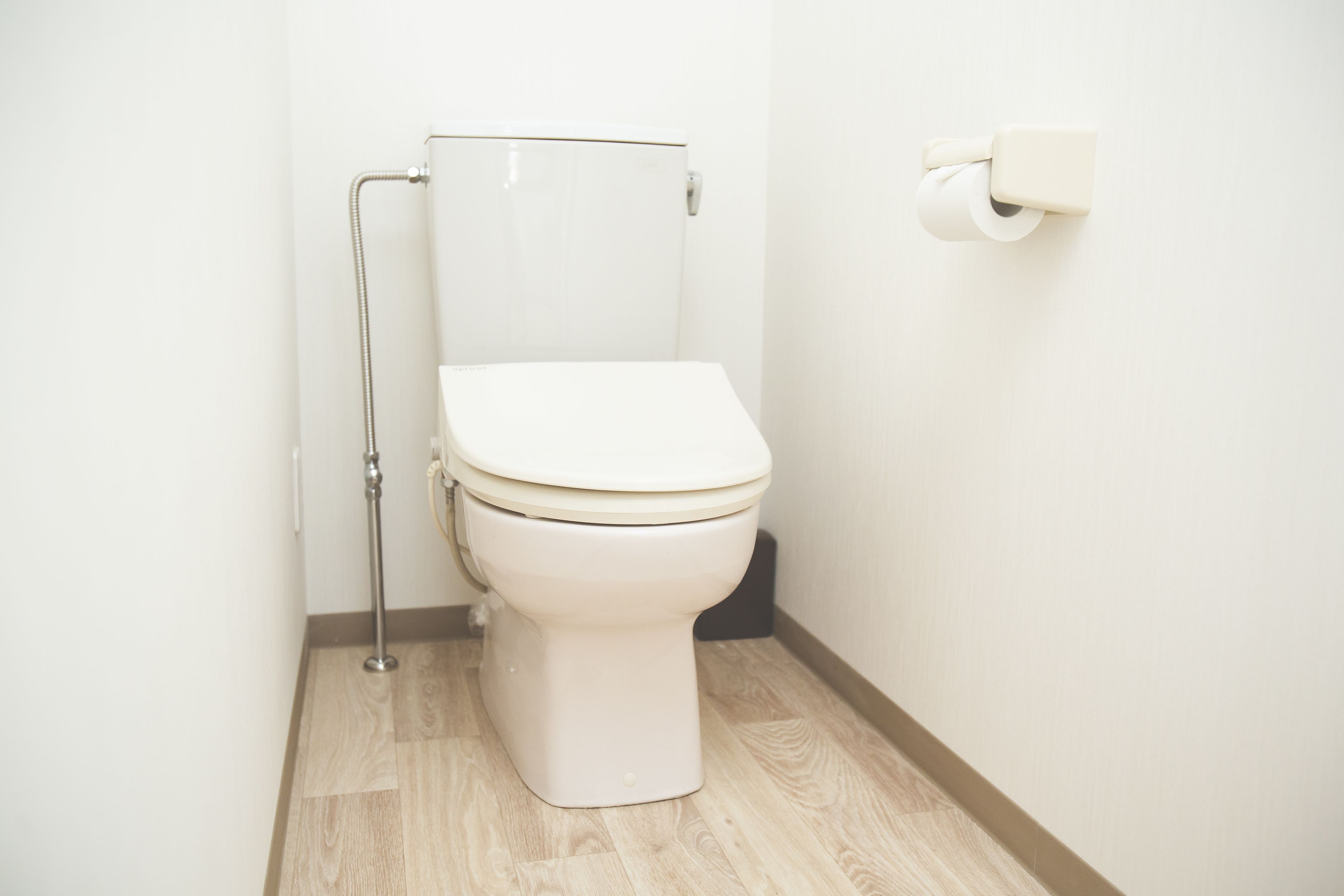 A white toilet with a flush handle and a toilet paper holder on the wall.