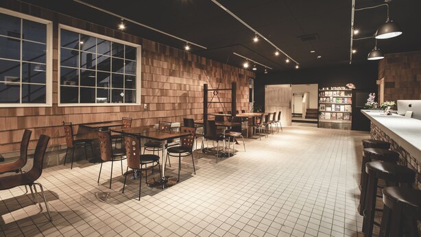 A restaurant with a modern interior, featuring wooden walls, tiled flooring, and a bar area with stools. - Noboribetsu Guest House AKA & AO - Hostel (Noboribetsu)