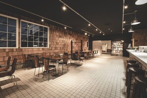 A restaurant with a modern interior, featuring wooden walls, tiled flooring, and a bar area with stools. - Noboribetsu Guest House AKA & AO - Hostel (Noboribetsu)