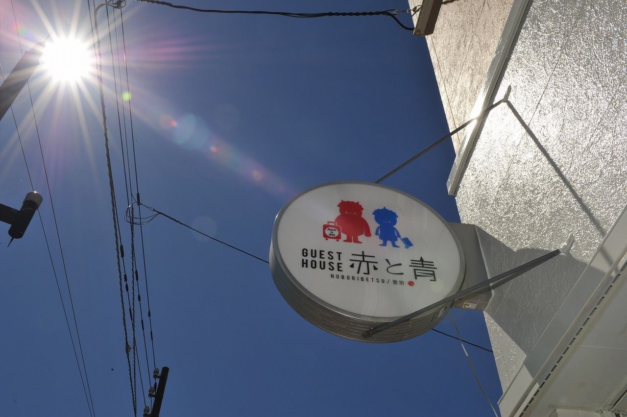 Cartell d'una casa de convidats amb una figura vermella i blava, i text en japonès.