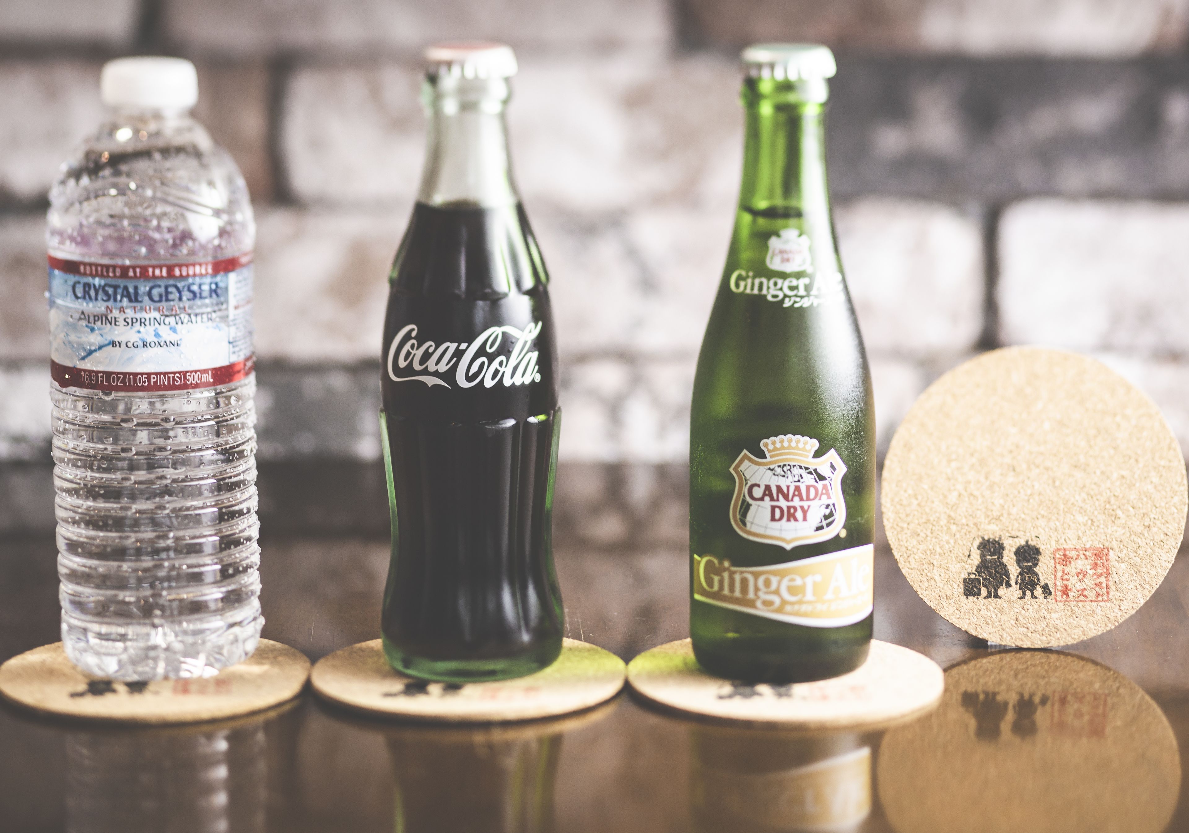 Three bottles of beverages on wooden coasters.