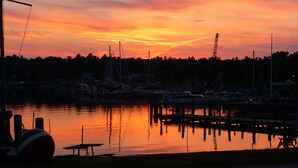 A marina at sunset with boats docked, a dock, and a beach area with a ball and a bench.