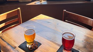 Una mesa de madera con dos vasos de cerveza, un letrero en una pizarra y vistas a un lago y árboles.