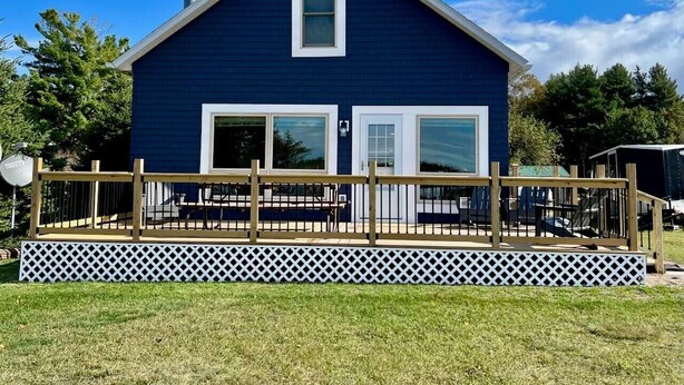 A blue house with a deck, a chimney, and a white fence.
