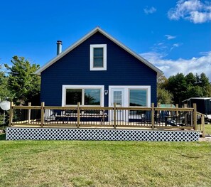 Une maison bleue avec une terrasse, une cheminée et une clôture blanche.