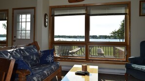 A living room with a wooden bench, a sofa with patterned cushions, a coffee table, and a view of a lake through large windows.