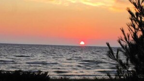 A sunset over the ocean with a silhouette of a boat and trees in the foreground.