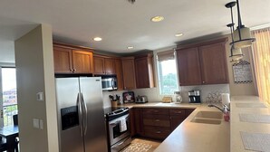 A modern kitchen with stainless steel appliances, wooden cabinets, and a large island with a sink. - Fantastic Penthouse Downtown Grand Haven! Harbor Front Views! Walk Everywhere! (Grand Haven)