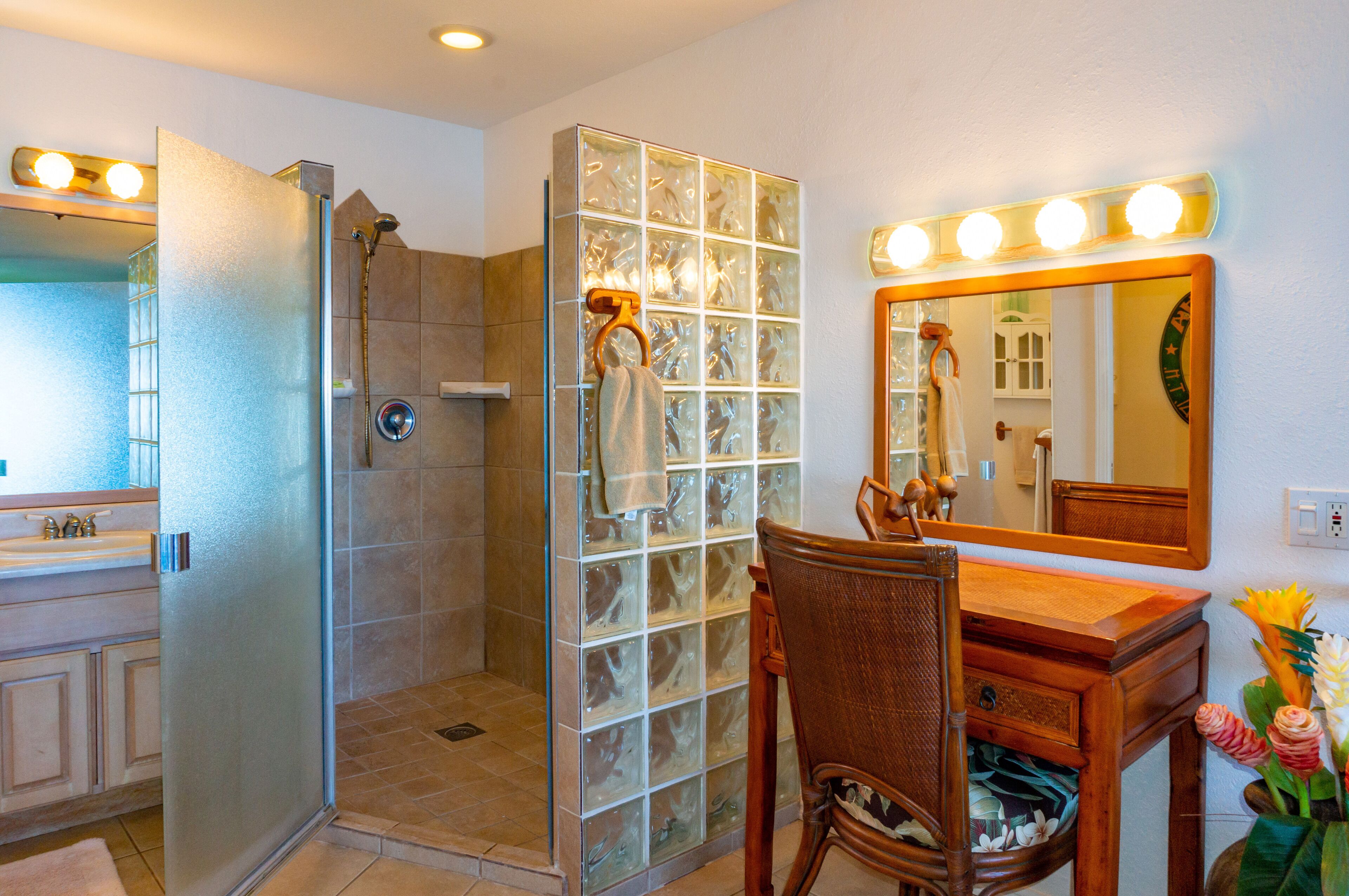 A bathroom with a glass shower enclosure, a vanity with a mirror, and a chair.