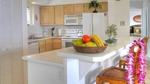 A kitchen with wooden cabinets, a microwave, a refrigerator, and a fruit bowl on the counter.