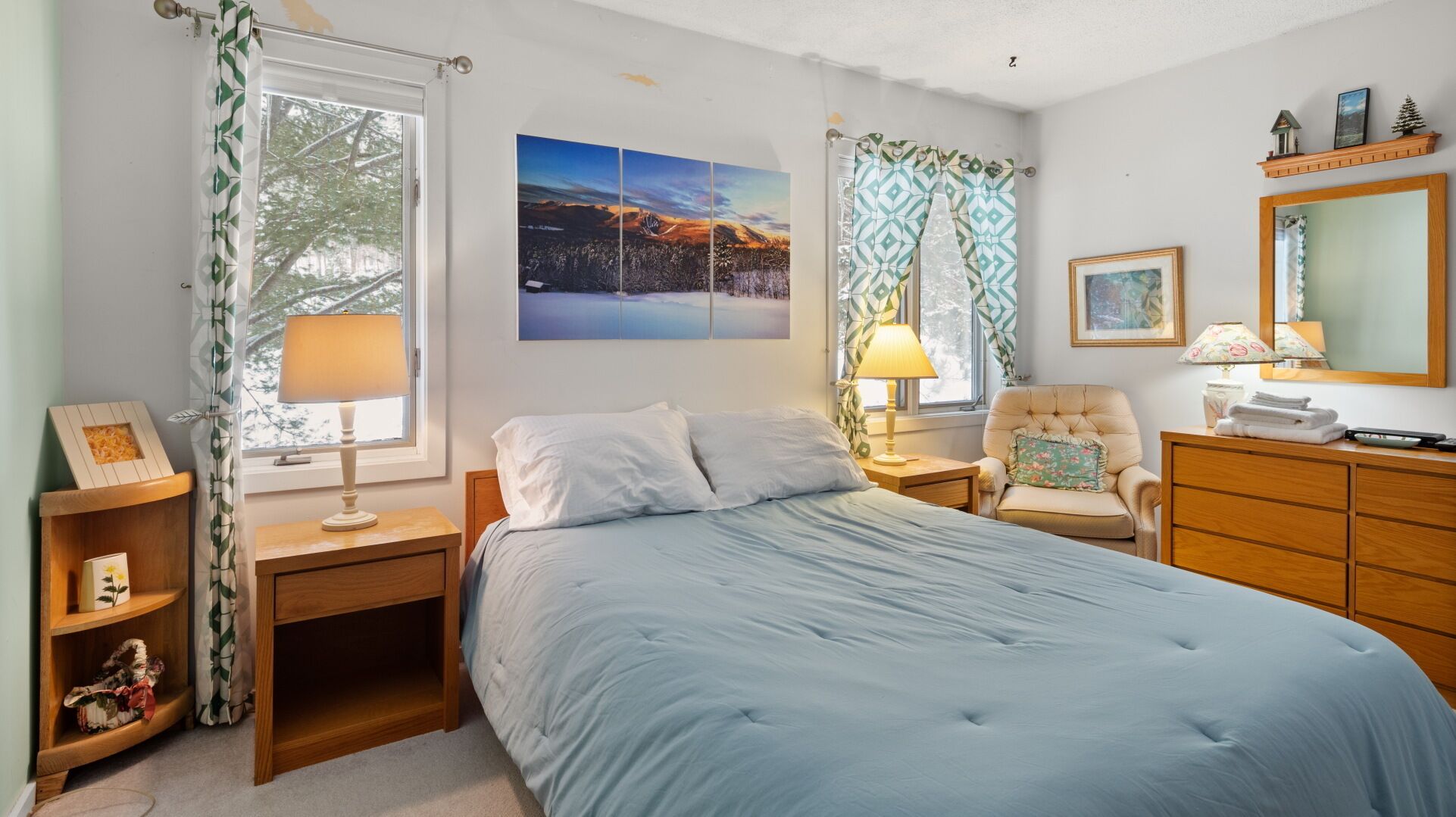 A bedroom with a bed, nightstands, a chair, a dresser, and a large window with curtains.