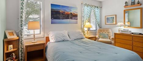 A bedroom with a bed, nightstands, a chair, a dresser, and a large window with curtains.