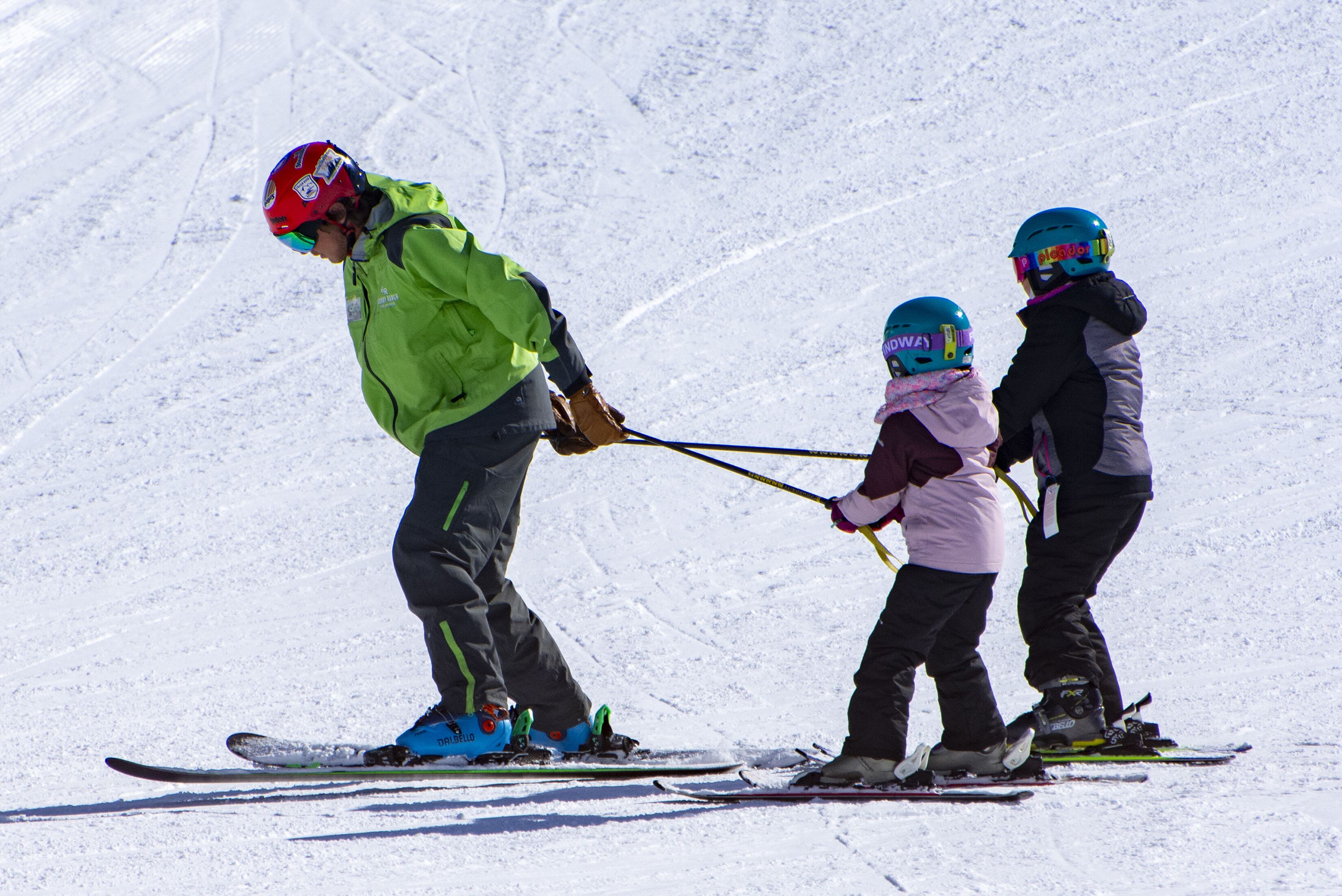 A person skiing with two children, all wearing helmets and ski gear.