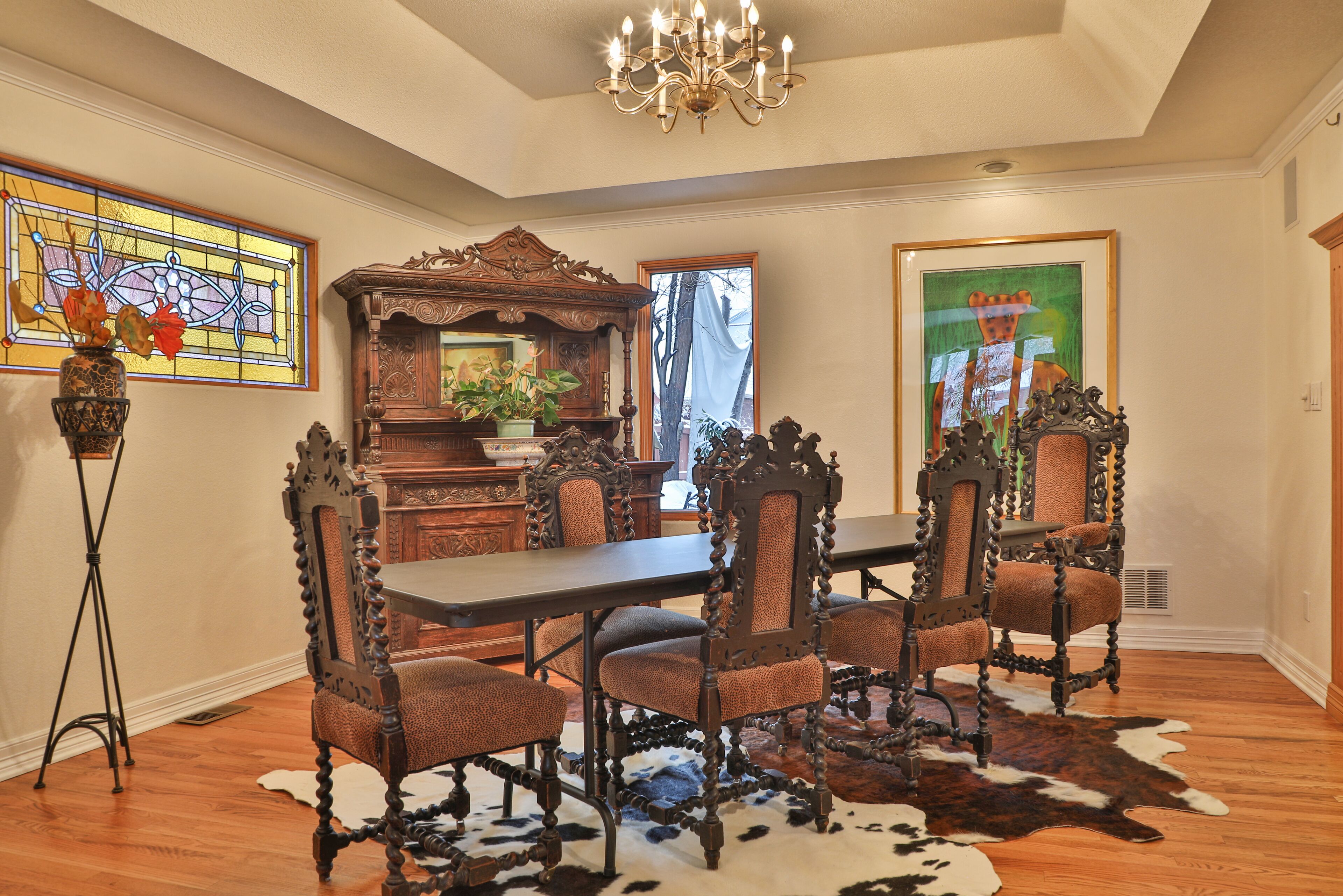 A dining room with a large wooden table, ornate chairs, a chandelier, and a cowhide rug.