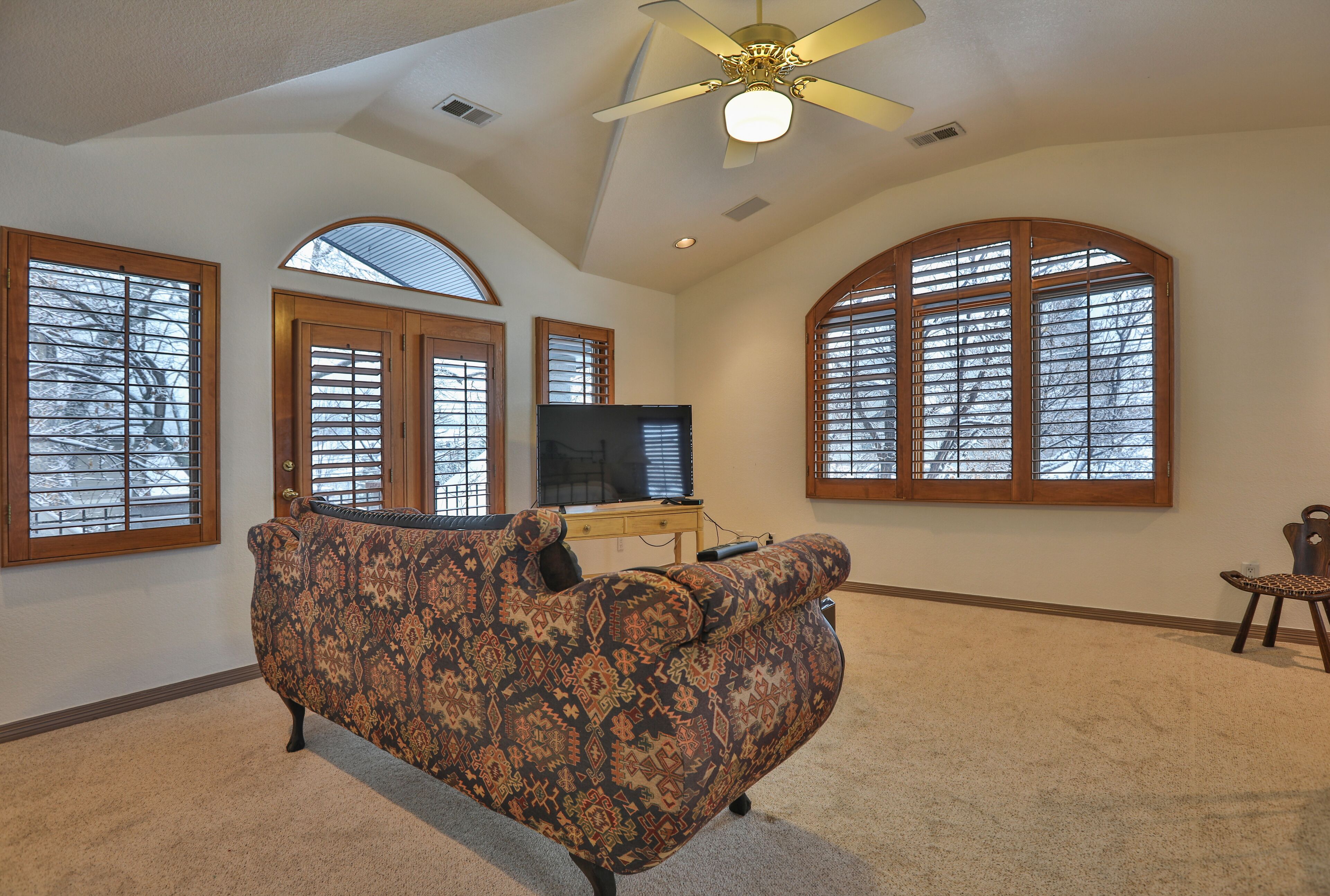 A living room with a patterned sofa, a television, and large arched windows.
