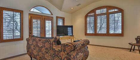 A living room with a patterned sofa, a television, and large arched windows.