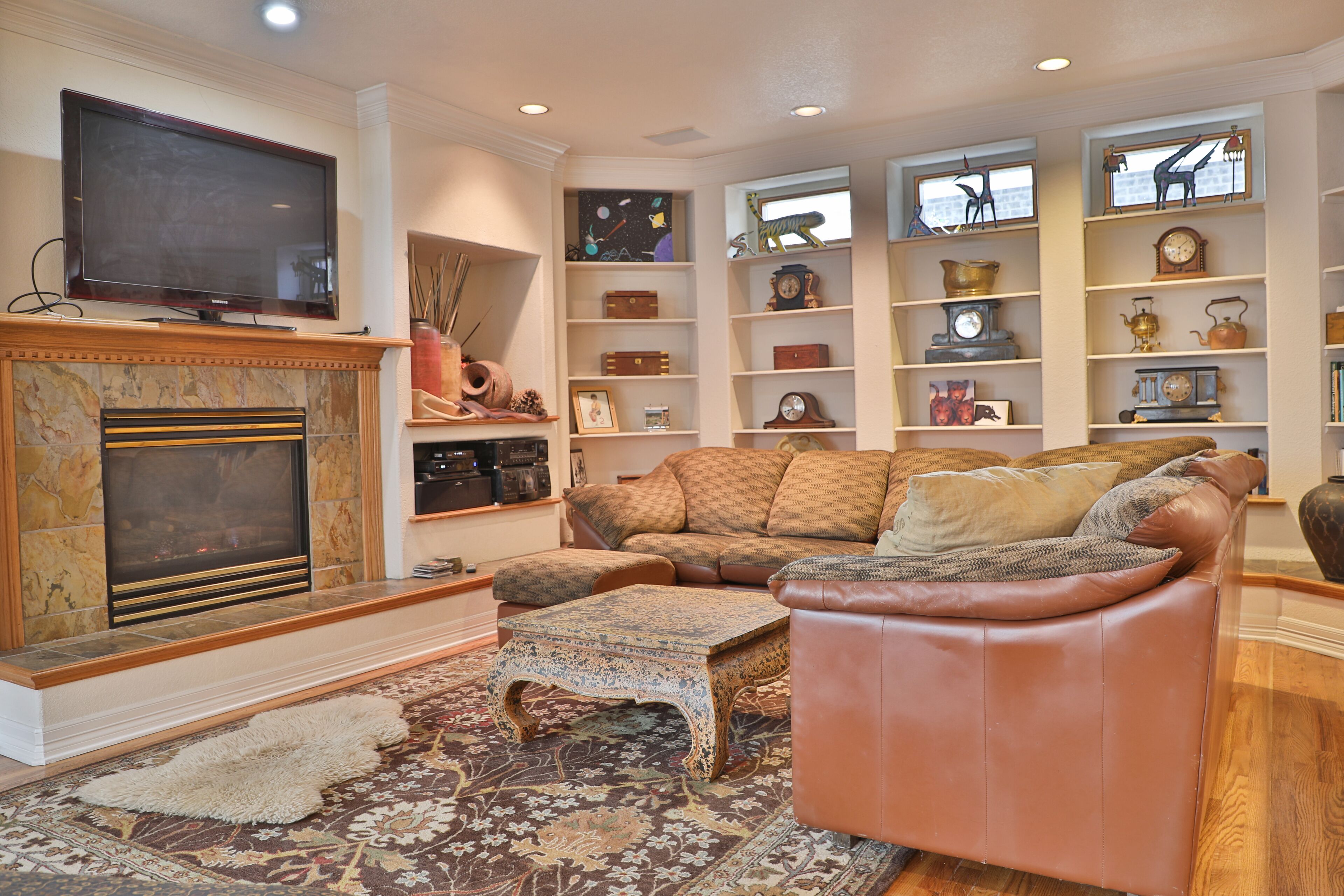 A living room with a fireplace, a television, a sofa, a coffee table, and a bookshelf filled with decorative items.