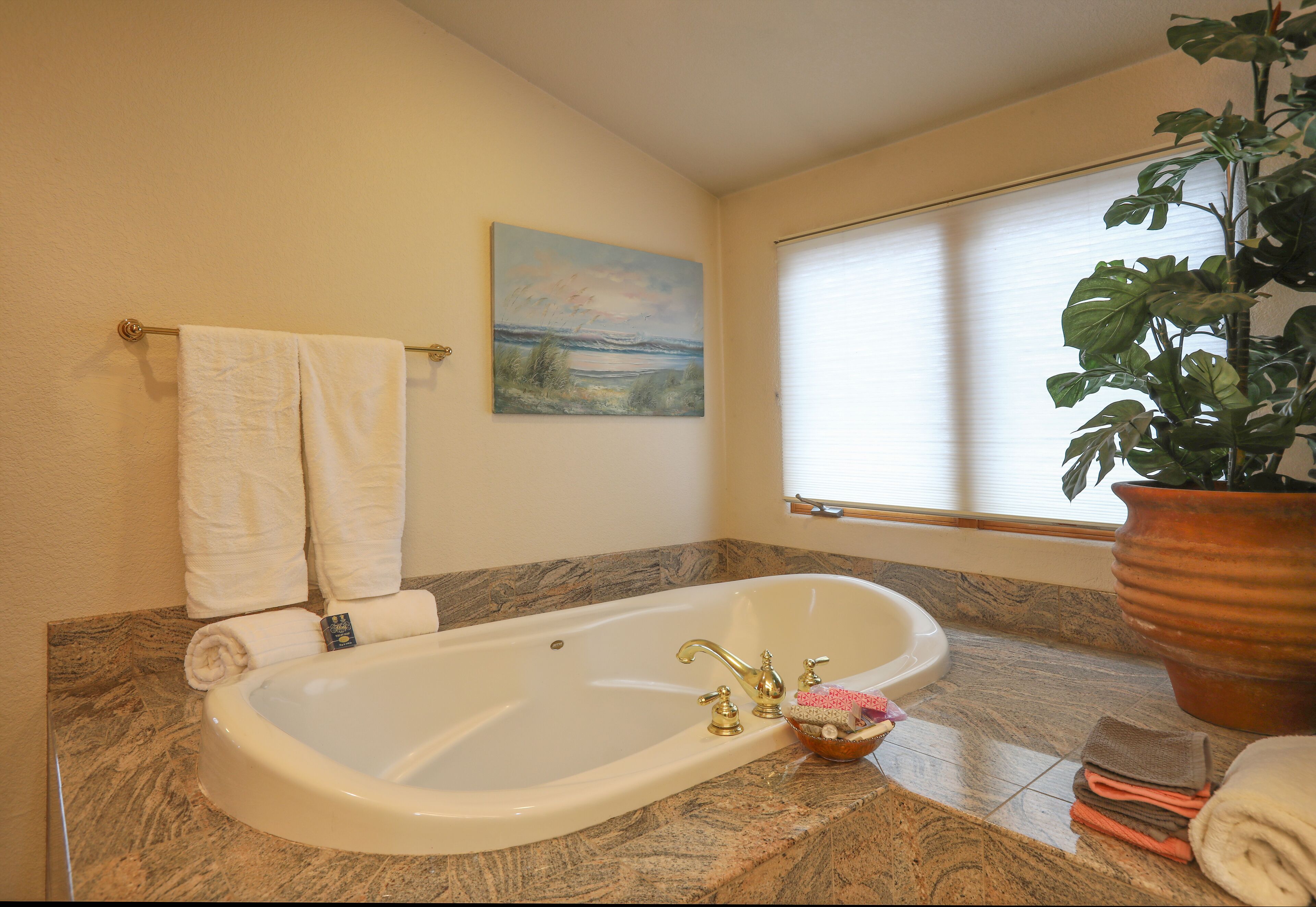 A bathroom with a bathtub, a painting on the wall, and a window with blinds.