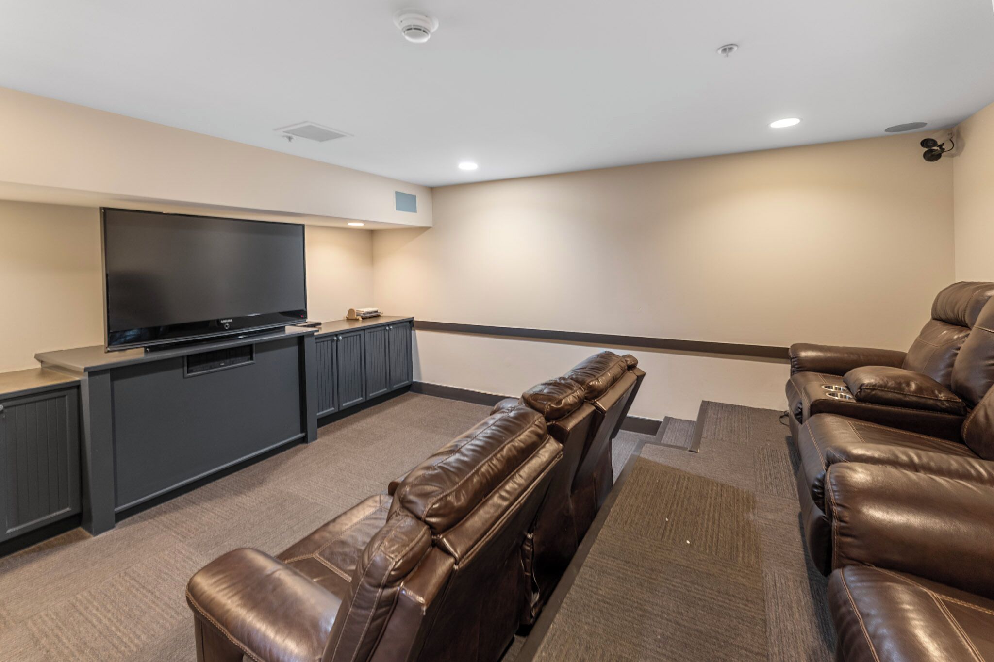 Un cine en casa con televisor de pantalla plana, sillones de cuero y piso alfombrado.