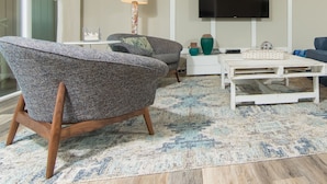 A modern living room with a flat-screen TV, two armchairs, a coffee table, and a patterned rug. - Oceanfront - 3 Bedroom Renovated 1,800 sq ft. + Huge Balcony -  Casual Elegance (St. Augustine Beach)