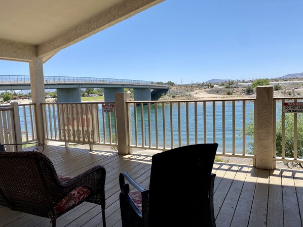A wooden deck with two wicker chairs, overlooking a river and a bridge.