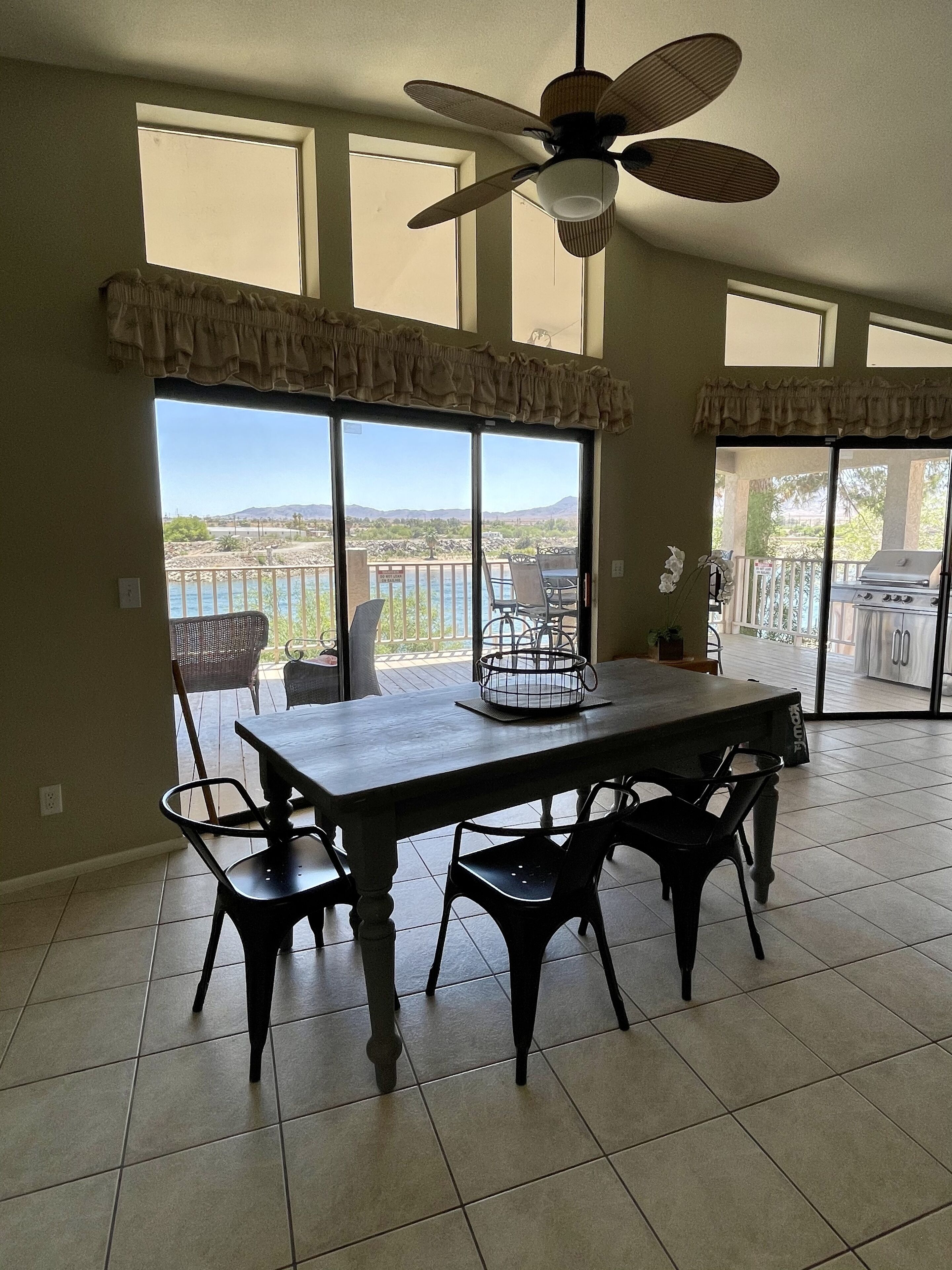 A dining area with a table and chairs, large windows with a view of the landscape, and a ceiling fan.