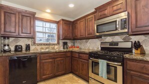 A kitchen with wooden cabinets, a stainless steel microwave, a stove, and a dishwasher. - Charming Brick Home Off Of Route 66 Near Tulsa Expo Fairgrounds. Sleeps 8 (Tulsa)