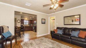 A living room with a black leather sofa, a wooden coffee table, and a fluffy rug. There is a ceiling fan and a framed picture on the wall. - Charming Brick Home Off Of Route 66 Near Tulsa Expo Fairgrounds. Sleeps 8 (Tulsa)