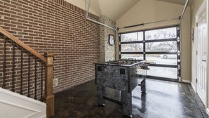 A room with a brick wall, a wooden staircase, and a foosball table. - Charming Brick Home Off Of Route 66 Near Tulsa Expo Fairgrounds. Sleeps 8 (Tulsa)