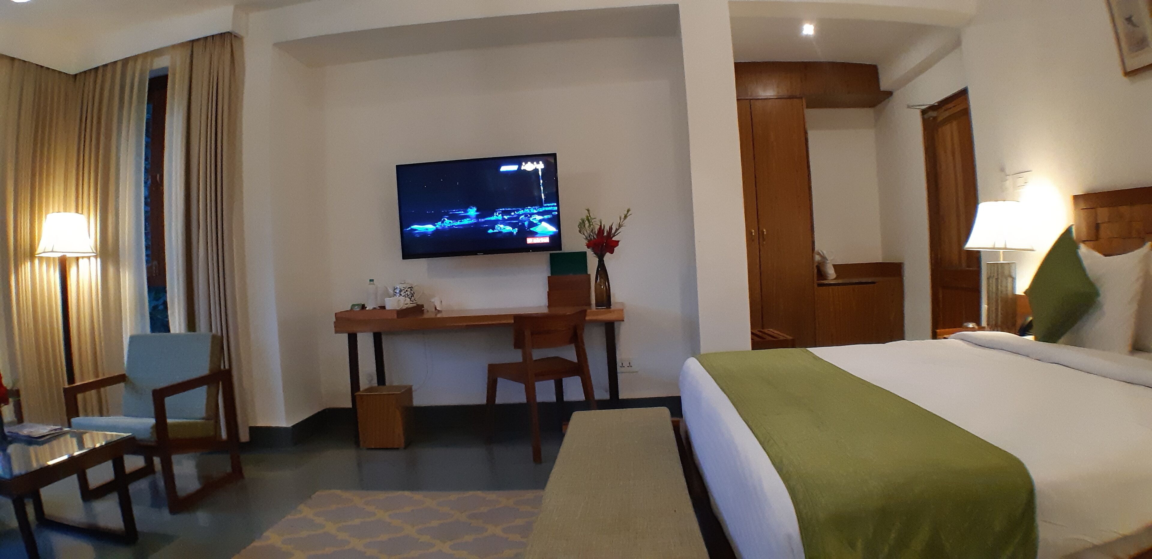 Una camera d'albergo con un letto, una scrivania, sedie, una televisione e una lampada.