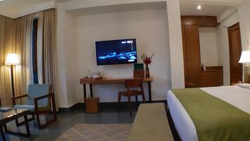 Habitación de hotel con cama, escritorio, sillas, televisor y lámpara.