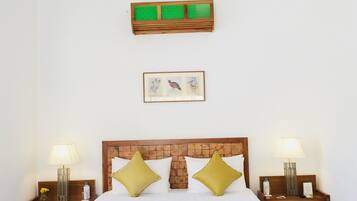Un cuarto de hotel ordenado con una cama grande, dos mesitas de noche, una lámpara colgante, un cuadro enmarcado y un adorno verde en la pared.