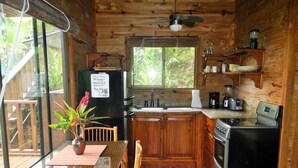 Una cabaña de madera con zona de cocina que incluye un refrigerador, estufa y cafetera. Hay una mesa de comedor con sillas y una planta encima.