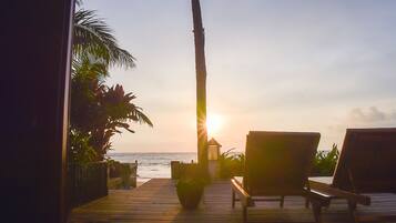 Terraza de madera con sillones de descanso y una pequeña estructura, con vista al océano al atardecer.