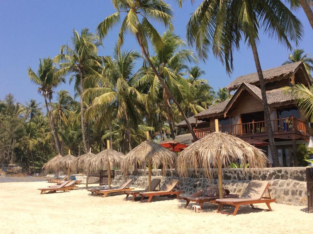 A beach with thatched umbrellas, wooden lounge chairs, and a building with a balcony.