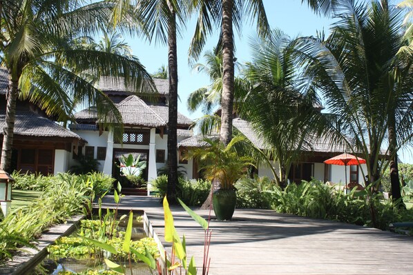 A resort with thatched-roof buildings, a wooden walkway, and lush tropical vegetation.