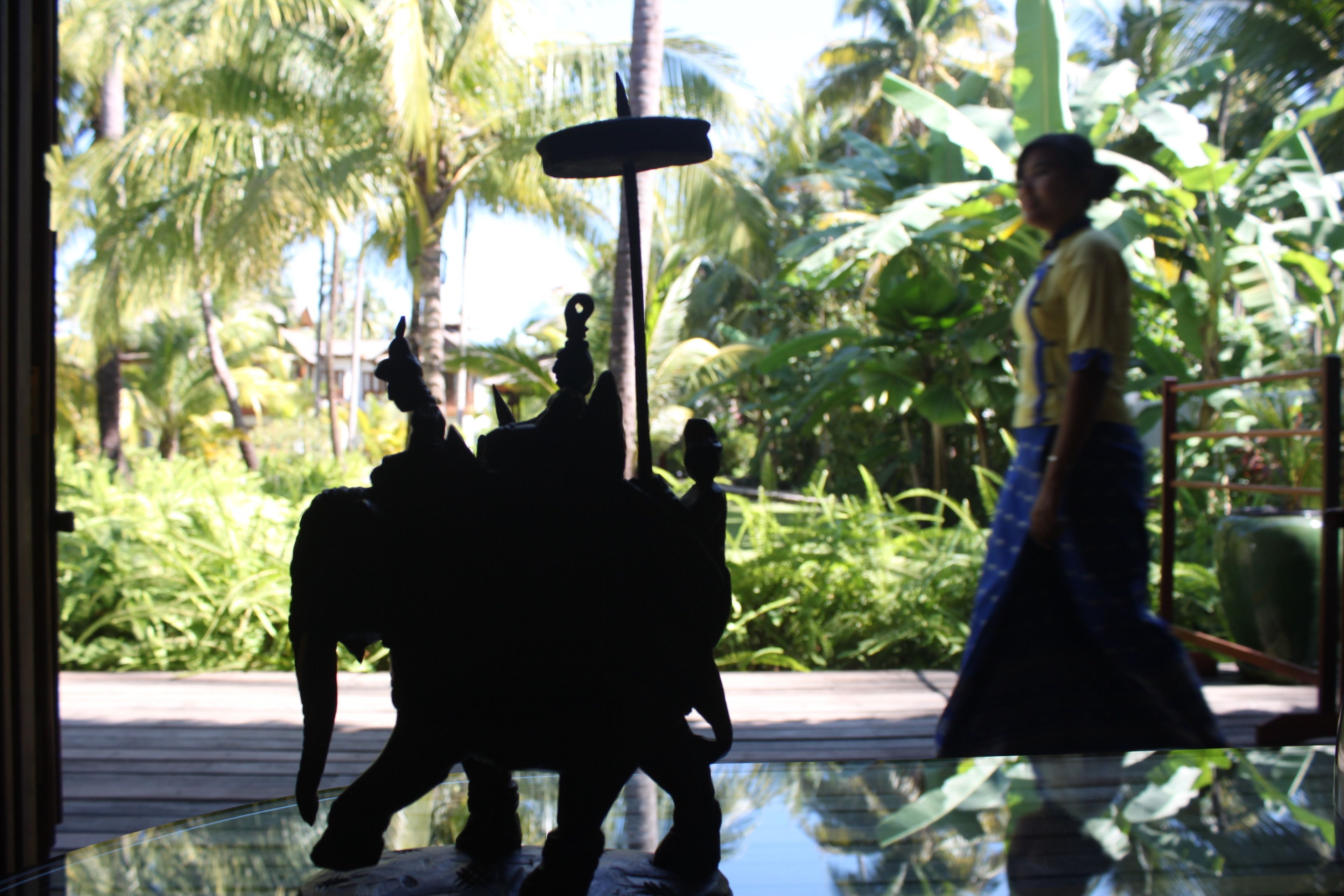 A statue of a figure with a staff, set against a backdrop of lush greenery and palm trees.