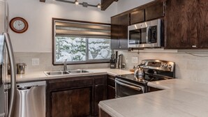 A modern kitchen with dark wooden cabinets, stainless steel appliances, and a window with a view of snow-covered trees. - Walk to Village Gondola. Updated 4BR 3 Bath for 2 families. Sleep 10. Fireplace. (Mammoth Lakes)