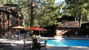 A pool area with a tiled deck, lounge chairs, and umbrellas. - Walk to Village Gondola. Updated 4BR 3 Bath for 2 families. Sleep 10. Fireplace. (Mammoth Lakes)